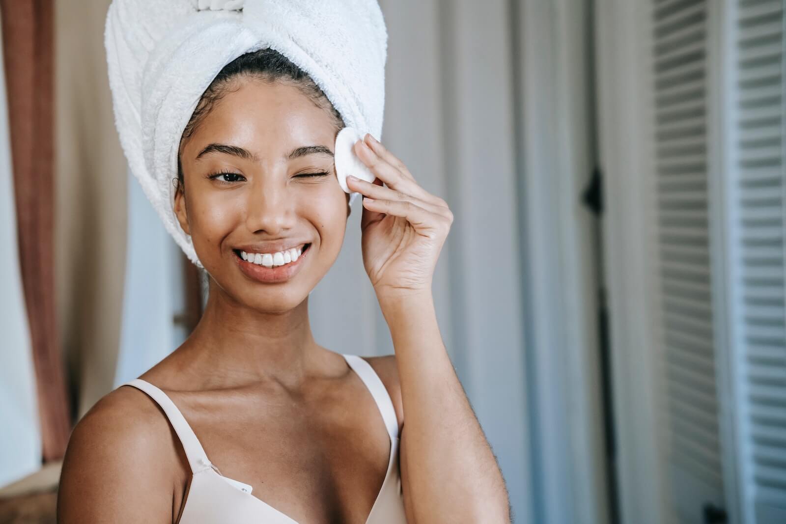 Mulher com toalha no espelho fazendo skincare.