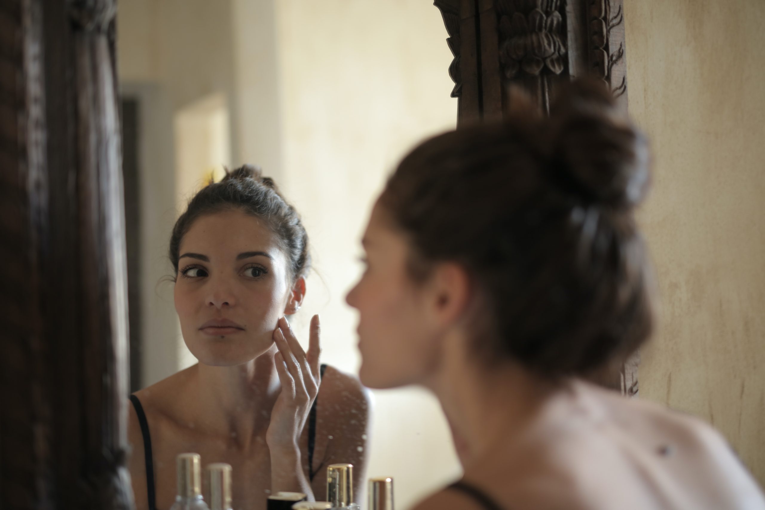 Ácido hialurônico | Mulher se olhando no espelho após rotina skincare